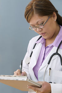 Picture of female Physician holding a pen while writing for a referral.
