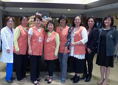 Picture of eight ladies one on the left has a white doctor coat and five in the middle have orange vest on and two on the far right has black dress jackets on.
