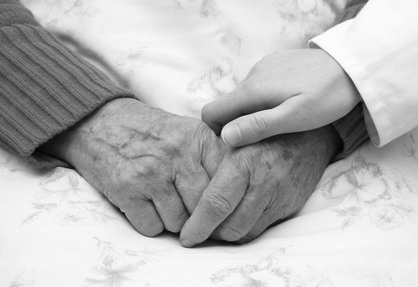 Picture of older persons hand being held by a nurses hand.
