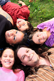 Picture of a family of five laying down, looking up at camera. Mother, father and three young daughters all smiling.
